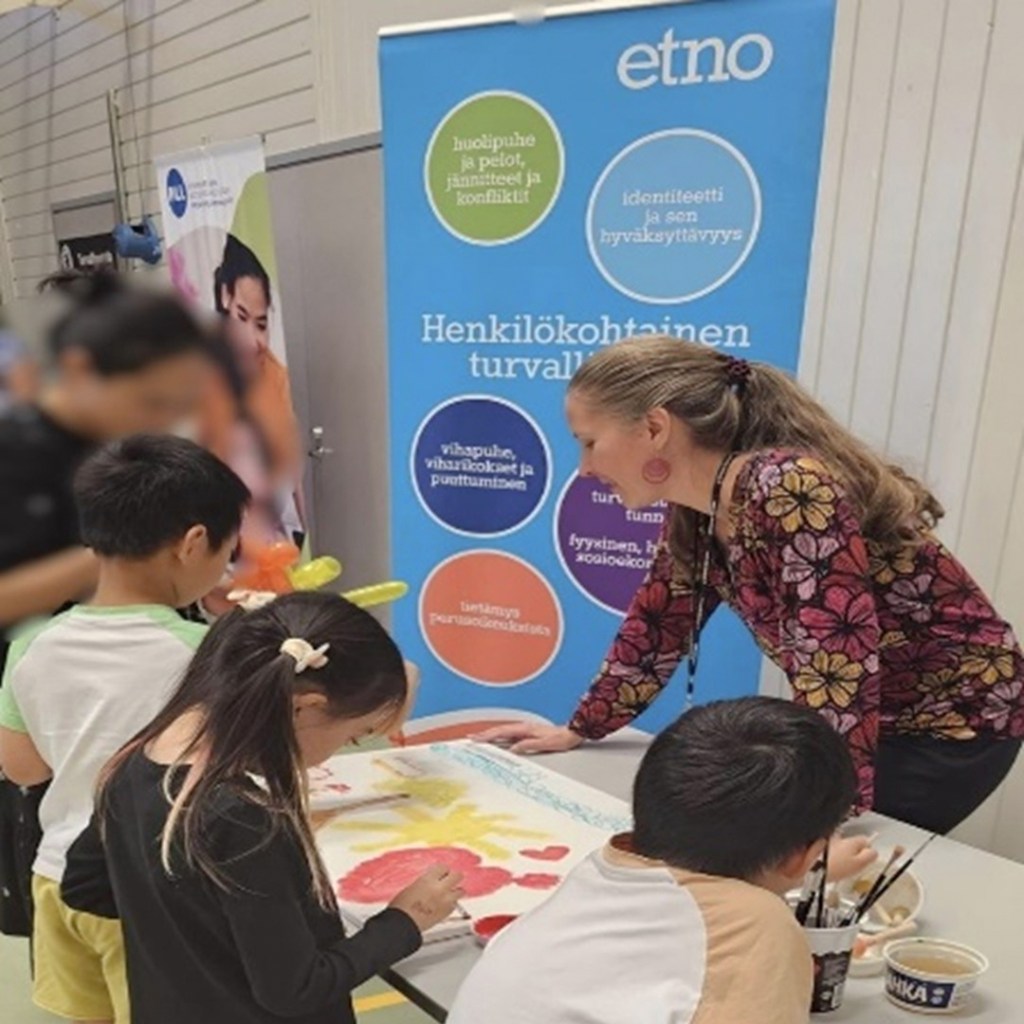 Maahanmuuttoasiantuntija perhetilaisuudessa, pöydän ympärille on kerääntynyt lapsia maalaamaan. 